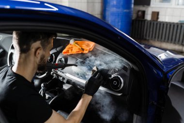 Buhar kullanarak arabanın içini köpükle ve deterjanla temizle. Otomotiv temizleme servisinde çalışan bir işçi. Araç iç dekorasyonu