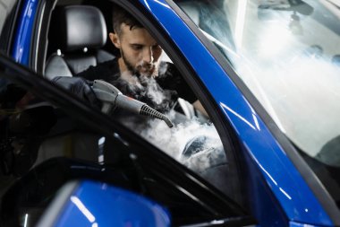 Arabanın içini temizliyorum. Hava sisteminde buhar temizliği. Otomotiv temizleme servisinde çalışan bir işçi.