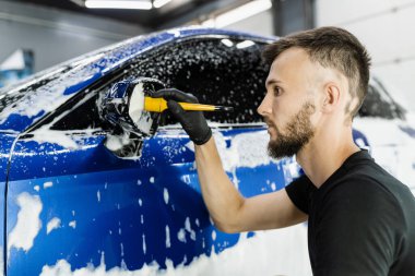 Araba temizleme servisinde el fırçasıyla araba yan aynasını köpükle yıka. Araba yıkama işçisi oto yıkama işi yapıyor.