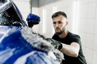 Mikrofiber eldivenle el yıkama ve garajda köpüklü araba gövdesi. Araba yıkama makinesi oto yıkama servisinde elle köpük yıkıyor.