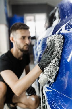 Araba yıkama makinesi oto yıkama servisinde elle köpük yıkıyor. Mikrofiber eldivenle el yıkama ve garajda köpüklü araba gövdesi.