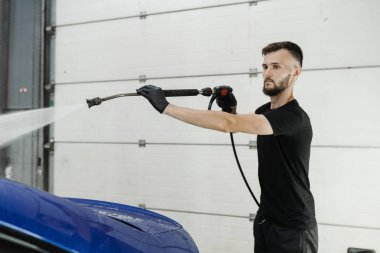 Garajda köpüğü temizlemek için arabaya su püskürtmek. Araba servisinde yıkama işlemi. Araba yıkama makinesi araba yıkama için su dolduruyor.