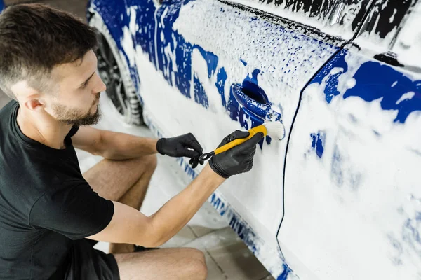 stock image Hand brush washing of car body with foam in car detailing service. Car wash worker washes a car body