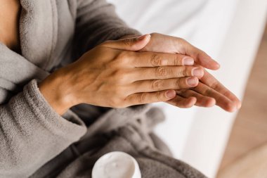 Afrikalı bir kız cildini yatak odasındaki kuraklıktan korumak için el nemlendirici kremi sürüyor. Elleri nemlendirici krem ile sabahları rutin güzellik yapan Afro-Amerikan kadın.