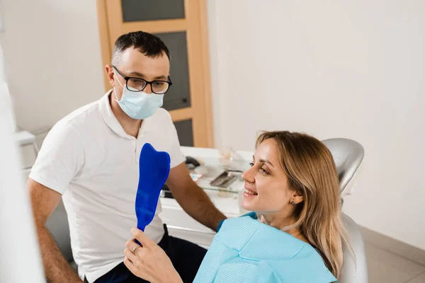 Dentist and woman patient in dentistry. Consultation with dentist at dentistry. Teeth treatment. Girl looking in the mirror at the dentist. Happy patient of dentistry