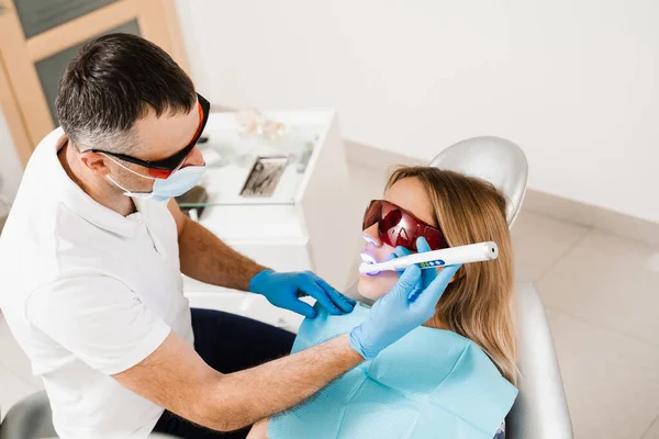 stock image Uv illumination of photopolymer tooth filling for woman in dentistry. Dentist in red protective glasses treats and removes caries of girl patient