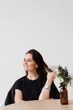 Mutlu, kendine güvenen bir kadın, beyaz arka planda, kafede oturuyor. Sıradan giyinmiş gülümseyen genç bir kadın yaşam tarzının tadını çıkarıyor.