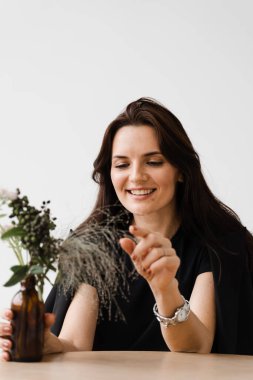 Mutlu, kendine güvenen bir kadın, beyaz arka planda, kafede oturuyor. Sıradan giyinmiş gülümseyen genç bir kadın yaşam tarzının tadını çıkarıyor.