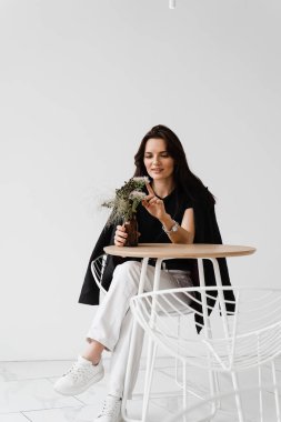 Sıradan giyinmiş gülümseyen genç bir kadın yaşam tarzının tadını çıkarıyor. Mutlu, kendine güvenen bir kadın beyaz arka planda, kafede oturuyor.