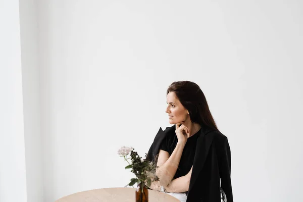 stock image Happy confident woman is sitting at table on white background indoor in cafe. Smiling young woman dressed casual business style enjoy her lifestyle