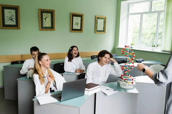 Schoolchildren at biology lesson at school with DNA model on the table. Biology teacher gives a lesson to pupils in classroom. Education at school of biology and chemistry