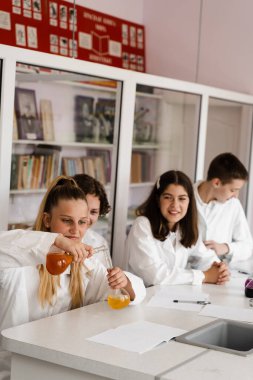 School education. Cheerful classmates in chemistry lesson hold flasks with liquid for experiments. Happy friends study together in class in laboratory