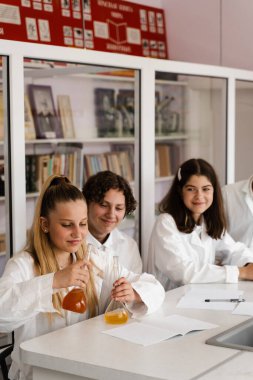 School education. Cheerful classmates in chemistry lesson hold flasks with liquid for experiments. Happy friends study together in class in laboratory
