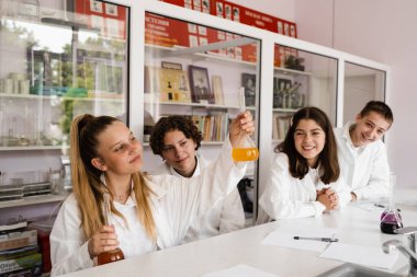 Chemistry lesson. Schoolgirl and classmates holds flask for experiments and smiles in the laboratory. School education