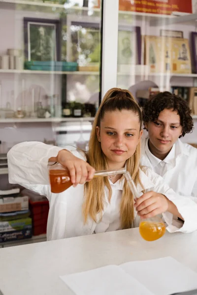 Chemistry lesson. Schoolgirl and classmates holds flask for experiments and smiles in the laboratory. School education
