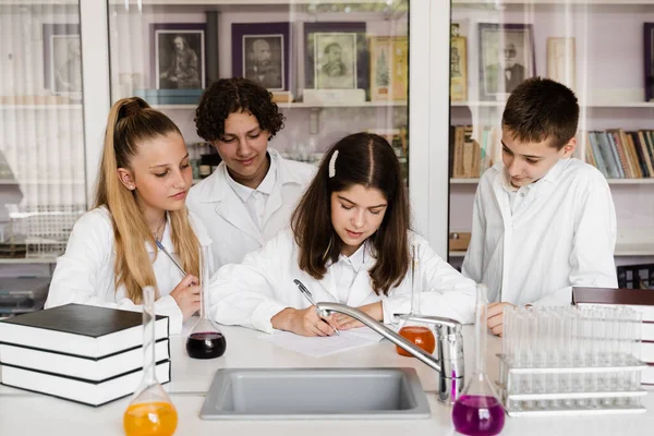 Discussion with a teacher at a chemistry lesson in a laboratory. Group of classmates are discussing chemistry experiments and homework at school. Education concept