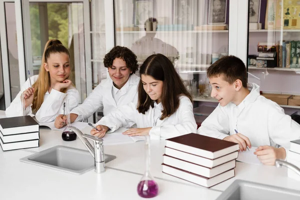 Discussion with a teacher at a chemistry lesson in a laboratory. Group of classmates are discussing chemistry experiments and homework at school. Education concept
