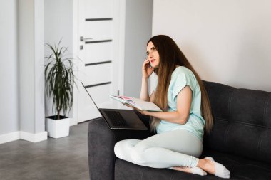 Evde çalışan dizüstü bilgisayarı olan meşgul kız. Genç iş kadını kanepede oturuyor ve yeni proje için yaratıcı fikirleri düşünüyor ve en iyi fikirleri fark ediyor.