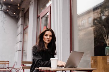 Bilgisayarlı çekici kız programcı, kafenin dışında, terasta çalışıyor. Başlangıç projesinde dizüstü bilgisayarla çalışan kendine güvenen genç iş kadını