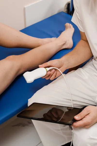 Portable ultrasound machine for ultrasound legs scanning. Vascular surgeon examines veins and arteries of legs using ultrasound machine of woman in medical clinic