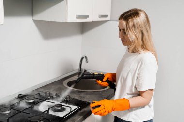 Woman housekeeper is steaming on cooker using steam generator. Steam cleaning of cooker in kitchen. Professional domestic cleaning service