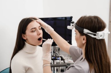 ENT doctor doing oropharyngoscopy procedure. Otolaryngologist examines woman throat with spatula. Consultation with laryngologist