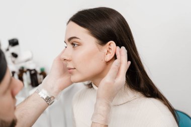 Otoplasty is surgical reshaping of the pinna, or outer ear for correcting an irregularity and improving appearance. Surgeon doctor examines girl ear before otoplasty cosmetic surgery clipart