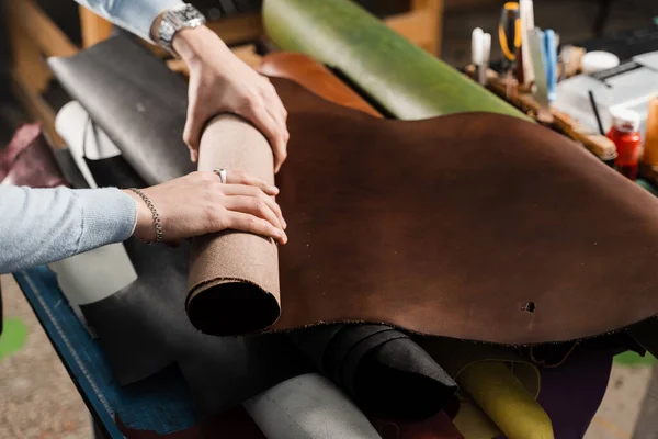 Leather craftsman is touching roll of genuine leather in the workshop. Rolls of genuine leather of different colors in leather products workshop