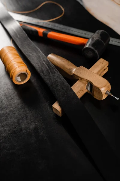 Genuine leather belt, thread, hammer and ruler. Tools of craftsman for belts creation. Equipment for genuine leather belt production on the table in the workshop