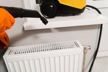 Professional cleaner is disinfecting heating radiator. Professional cleaning service cleans dirt and dust at home. Steam cleaning of heating battery at home