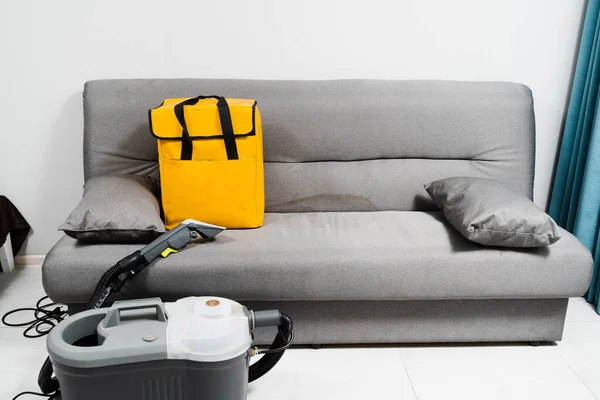 Extractor dry cleaning machine for removing stains and dirt from couch at home. Professional cleaning service. Professional dry cleaning machine and yellow transport bag