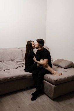 Man in love hug and kiss his girlfriend in cozy house. Young family spending time together. Feelings and love. Love story of beautiful young couple spending time together at home on the couch