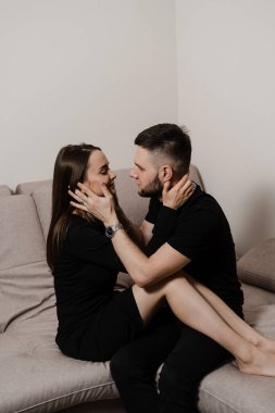 Love story of a couple spending time in cozy room at home. Relationships, feelings and tenderness in the family of men and girl. Couple in love hugging and kissing on couch at home