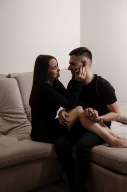 Love story of a couple spending time in cozy room at home. Relationships, feelings and tenderness in the family of men and girl. Couple in love hugging and kissing on couch at home