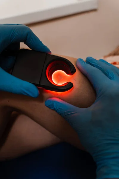 Vascular surgeon examines leg veins of woman using led venous scanner with red illumination. Venous led scanner for helping to locate the veins
