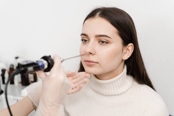 ENT doctor otolaryngologist with headlight treat nose woman patient. Nose endoscopy. Rhinoscopy procedure with rhinoscope