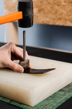 Craftsman is punching genuine leather using line punch and hammer for creation natural leather products. Tools of craftsman for belts creation. Equipment for genuine leather production in workshop