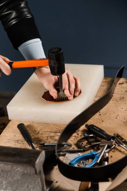 Craftsman is punching genuine leather using line punch and hammer for creation natural leather products. Tools of craftsman for belts creation. Equipment for genuine leather production in workshop