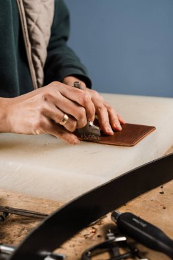 Craftsman is punching genuine leather using line punch and hammer for creation natural leather products. Tools of craftsman for belts creation. Equipment for genuine leather production in workshop