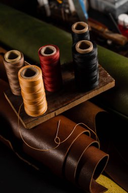 Needle with spools of thread on roll of brown genuine leather in craftsman workshop. Handmade genuine leather production in the factory
