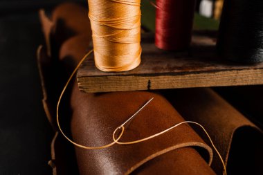 Close-up thread with needle on roll of brown genuine leather in craftsman workshop. Handmade genuine leather production in the factory