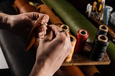 Craftsman sews genuine leather using needle and thread for creation natural leather products. Equipment for genuine leather production in workshop. Process of stitching genuine leather