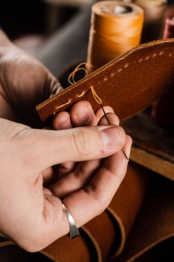 Craftsman sews genuine leather using needle and thread for creation natural leather products. Equipment for genuine leather production in workshop. Process of stitching genuine leather