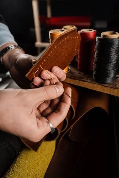 Craftsman sews genuine leather using needle and thread for creation natural leather products. Equipment for genuine leather production in workshop. Process of stitching genuine leather