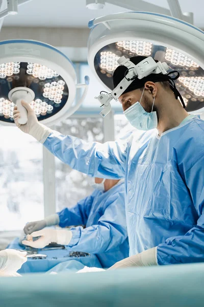 Male surgeon is holding light lamp in the operating room and directs it to the operating field. Surgeon with headlight is preparing for surgery in medical clinic