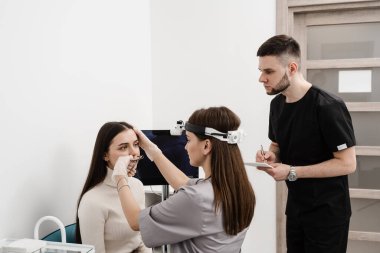 Consultation with ENT doctor. Otolaryngologist with colleague examines girl nose before procedure of endoscopy of nose. Rhinoscopy of woman nose