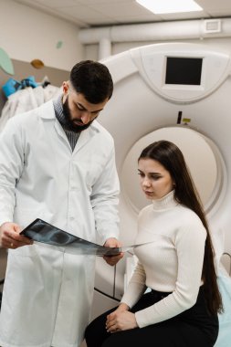CT scan radiologist showing x-ray of abdomen to girl patient in computed scanning room. CT Doctor consulting patient and showing chest x-ray to patient in computed tomography room