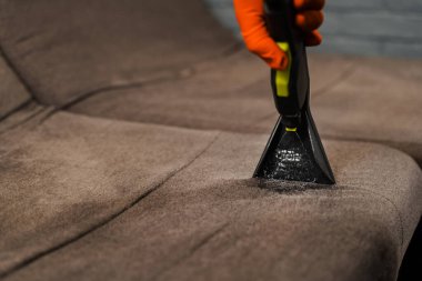 Dry cleaning extractor machine is spraying water and detergent close-up. Professional domestic cleaning service worker is removing dirt and dust from couch using dry cleaning machine