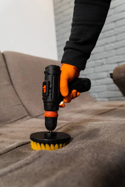 Applying detergent on couch for dry cleaning using extractor machine. Close-up process of dry cleaning for removing stains and dirt from couch at home. Professional cleaning service