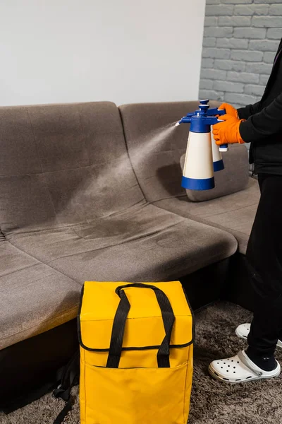 Spraying detergent on couch for dry cleaning using extractor machine. Process of dry cleaning for removing stains and dirt from couch at home. Professional cleaning service